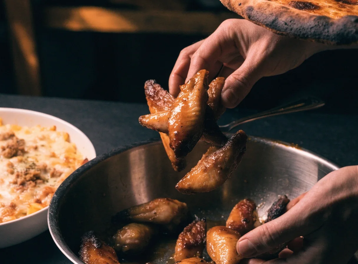 Roasted wings and baked pasta beside pizza on a dark table