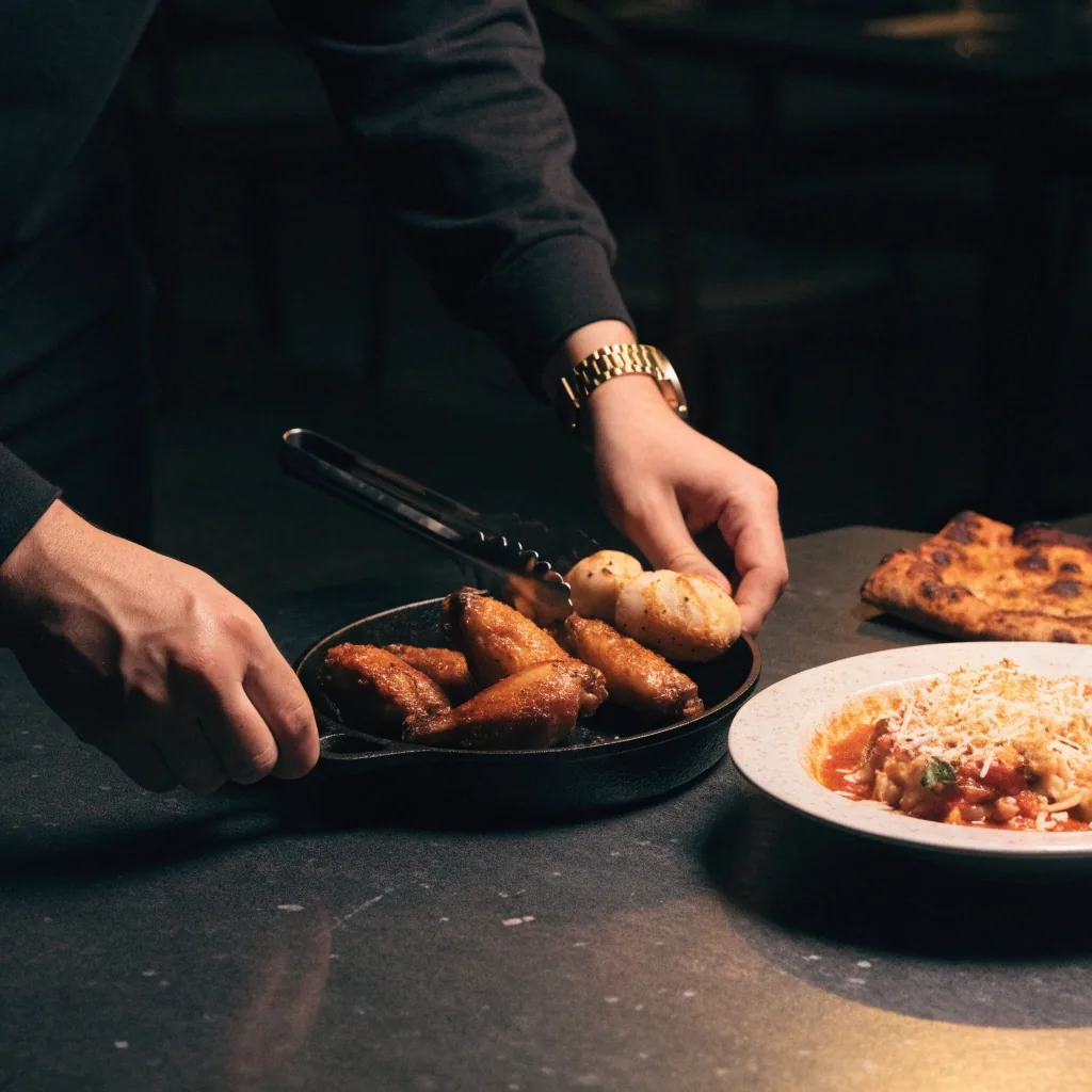 Coal-fired pizza, roasted wings and pasta on a dark stone table